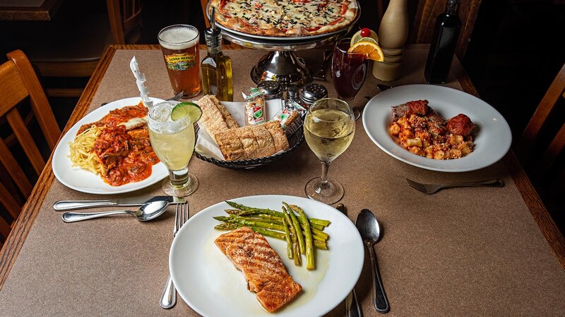 Table with multiple entrees and pizza pie with focus on salmon entree with asparagus